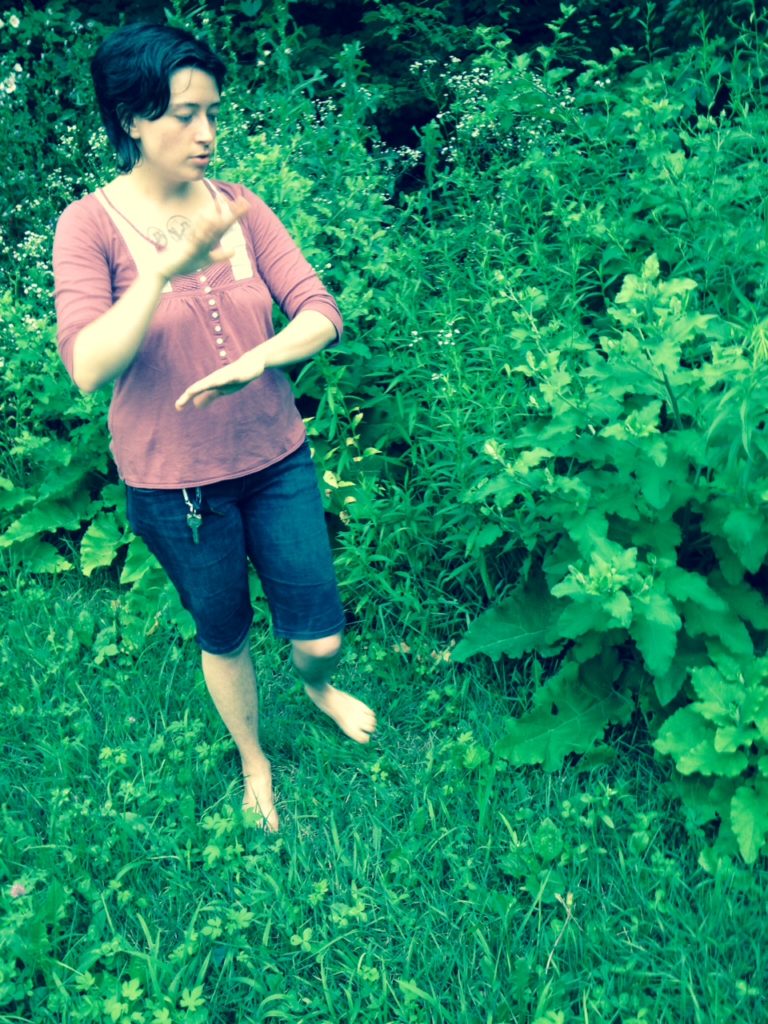 barefoot white woman standing in a community garden, gesturing about the size of the burdock plants